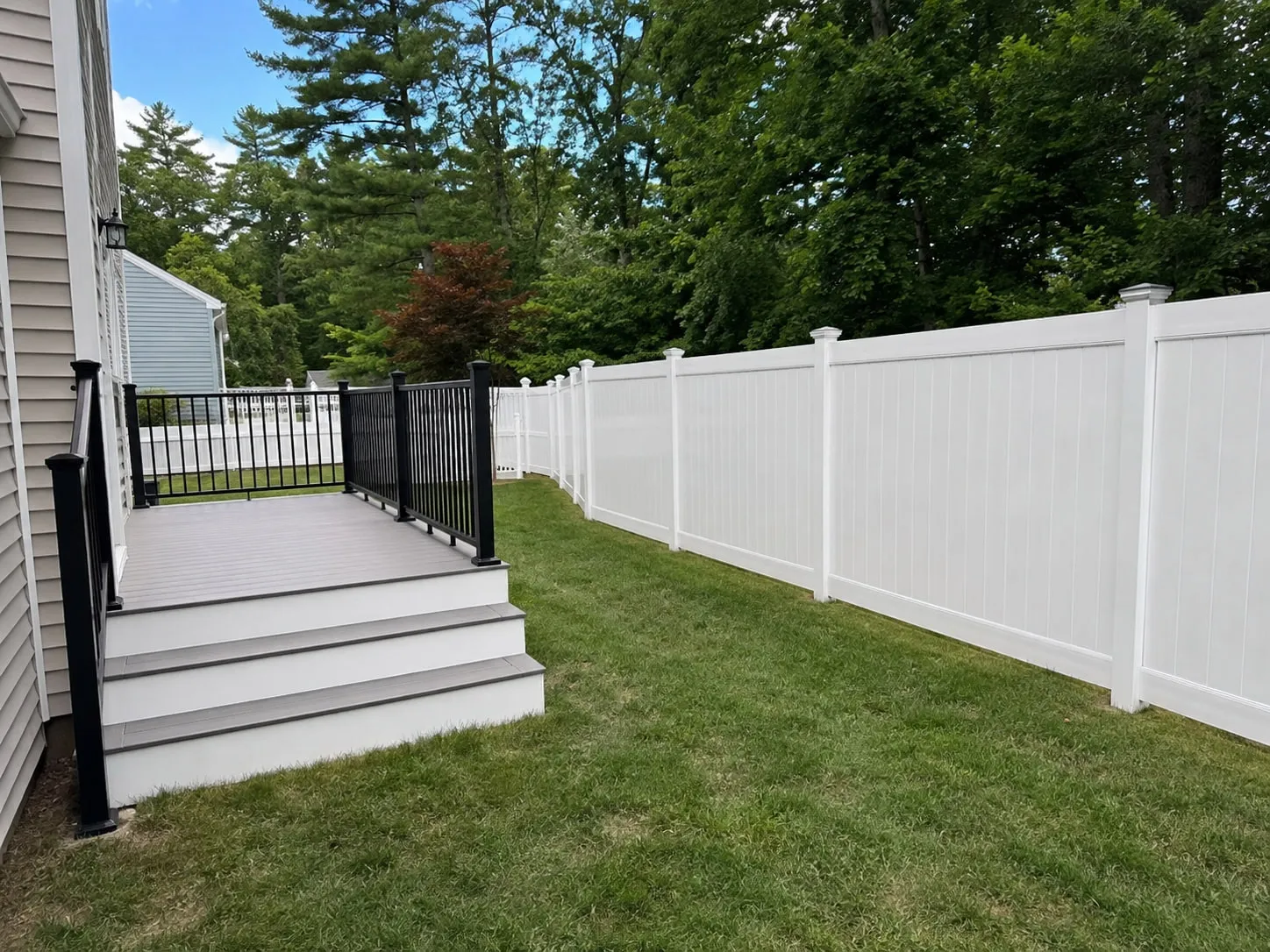 Composite deck with black railings beside a new white vinyl privacy fence in the same backyard
